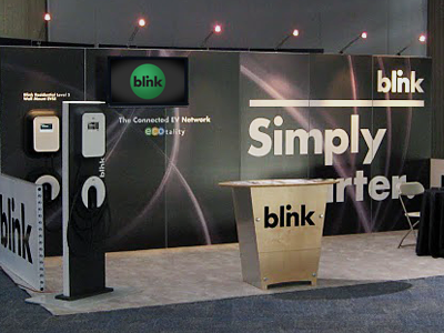 Tradeshow Booth Design Variation black fade effect blink network ecotality ev charger gray and black design green circle lighting for trade show booth trade show booth design trade show design tv screen on trade show booth white and black design wood table with logo