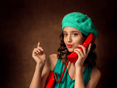 A girl in a green dress and green beret is talking on a red pho