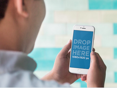 Man Holding an iPhone Over a Blue Tiled Wall Mockup Template