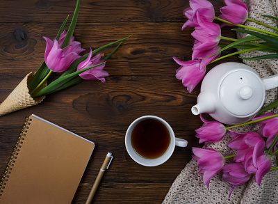 Tulips, a notebook, a white teapot and a cup of tea are laid out design typography