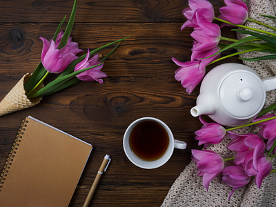 Tulips, a notebook, a white teapot and a cup of tea are laid out