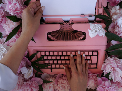 Women's hands are typing on an old typewriter among peonies design