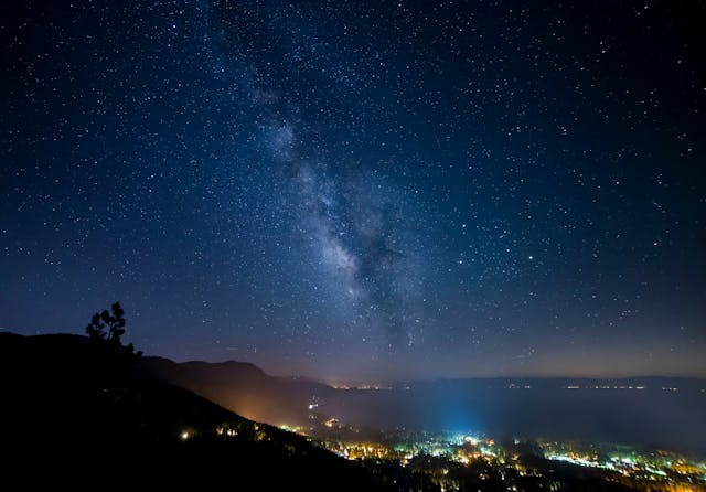 Paisagem mostrando a cidade vista de cima, aos pés de uma montanha e um lindo céu estrelado