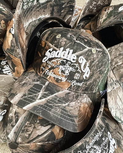 Saddle Up • Camo Hats apparel christian cowboy embroidery horse howler hunting illustration merch nature outdoors realtree rodeo seager sendero sky typography western